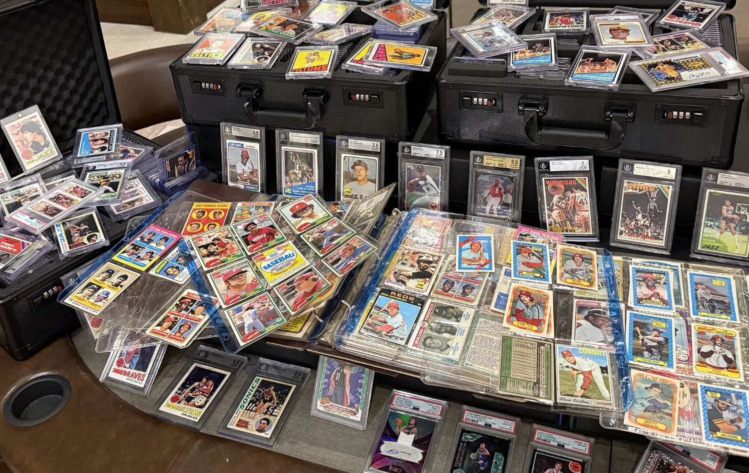 Two binders open on the table, their nine-pocket pages full of 1970s and &rsquo;80s baseball cards, with graded basketball cards standing behind them.
